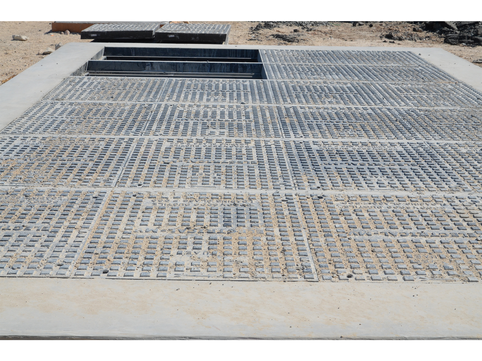 Large multi-part ductile iron access cover set in a concrete surround, with covers lifted at one end to show the removable support beams beneath